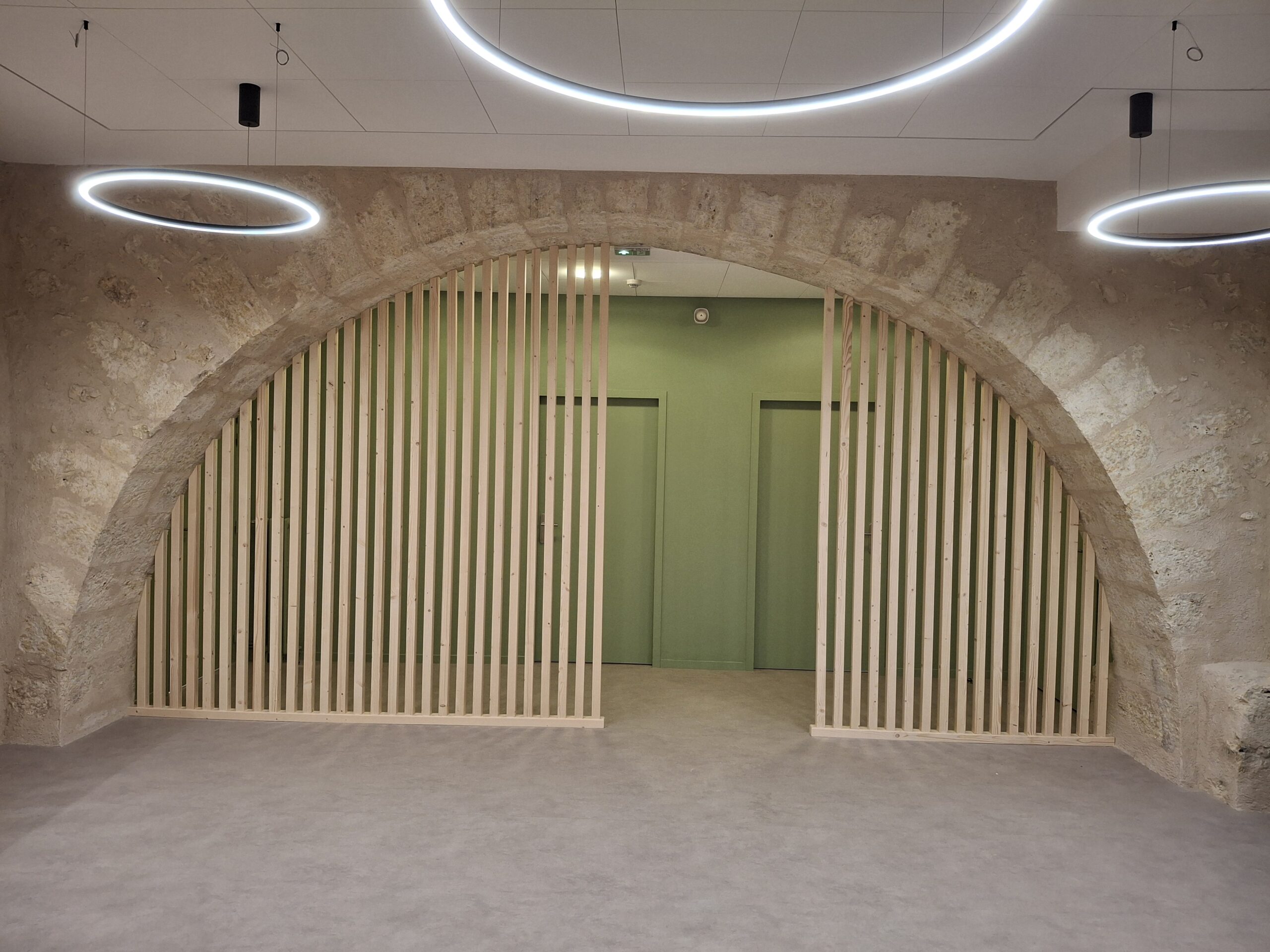 Espace contemporain signé Menuiserie MDB en Occitanie, arche en pierre, lattes bois et portes vert pâle,